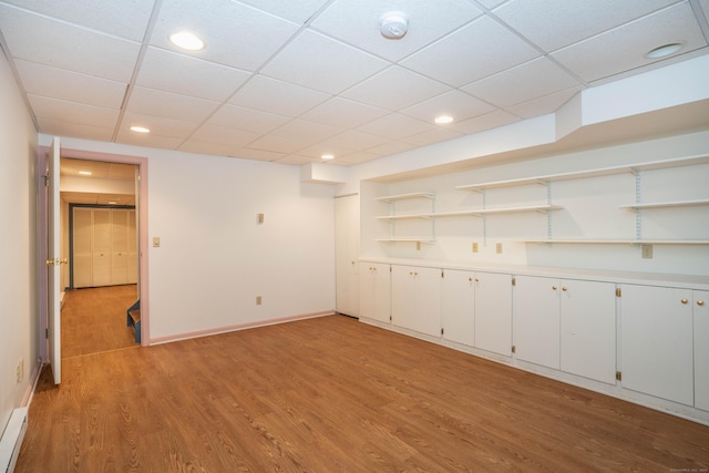 basement with a drop ceiling, light hardwood / wood-style floors, and built in features