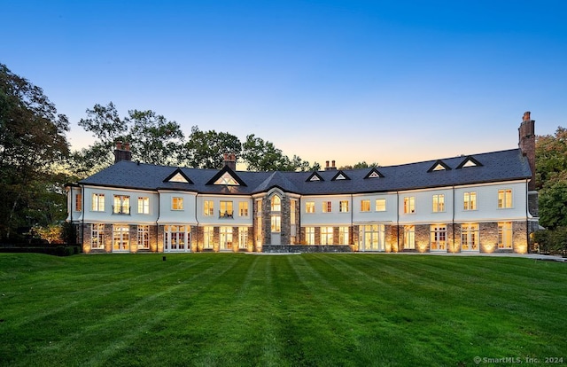 back of property at dusk with a lawn and french doors