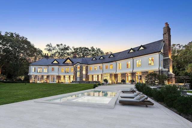 back of property at dusk featuring a lawn, an in ground hot tub, and a chimney