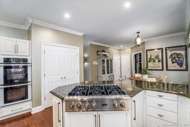 kitchen with dark stone countertops, stainless steel appliances, dark hardwood / wood-style floors, white cabinets, and ornamental molding