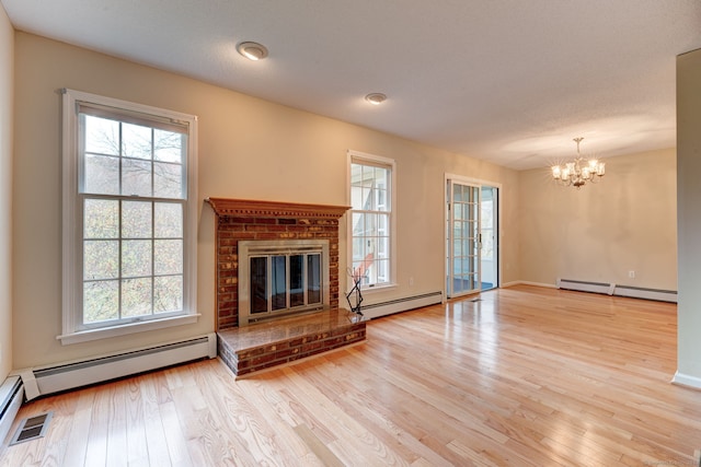 unfurnished living room with baseboard heating, light hardwood / wood-style flooring, a notable chandelier, and a fireplace