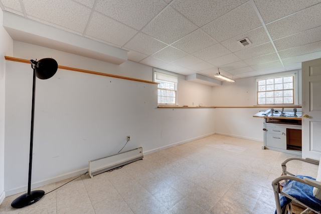 basement with a drop ceiling, a healthy amount of sunlight, and a baseboard radiator