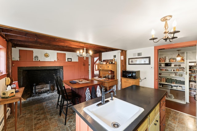 kitchen featuring dark countertops, an inviting chandelier, a fireplace with flush hearth, and a sink