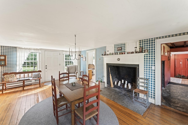 dining space with a fireplace, wallpapered walls, a chandelier, and hardwood / wood-style flooring