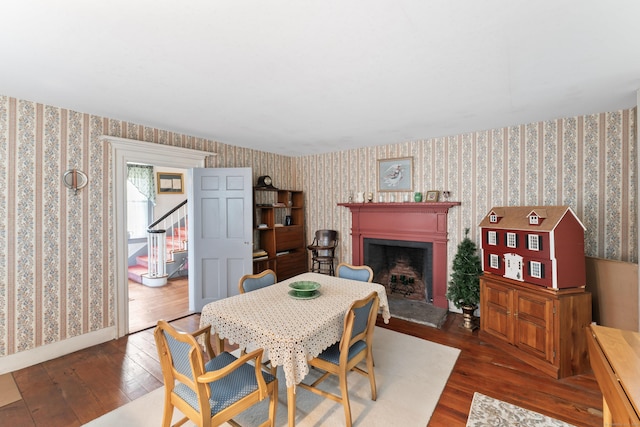 dining room with wood-type flooring, wallpapered walls, and a fireplace with raised hearth