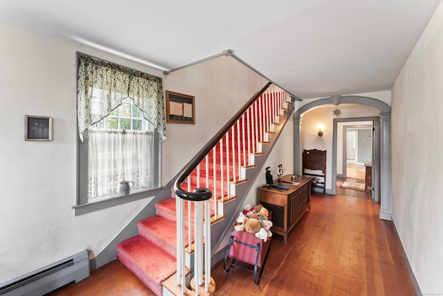 staircase with decorative columns, wood-type flooring, and baseboard heating