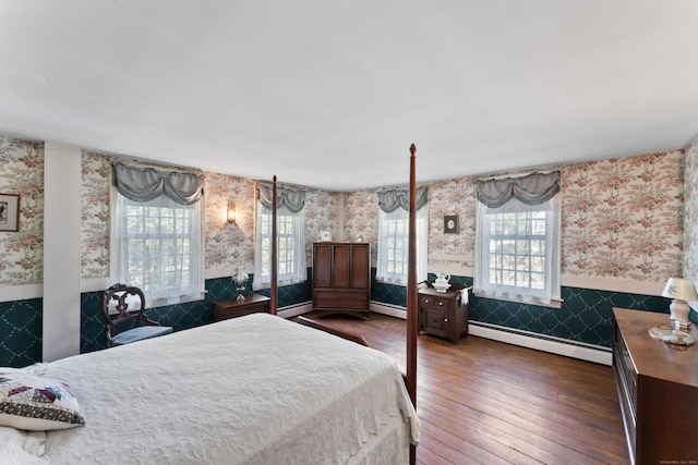 bedroom featuring baseboard heating, wainscoting, hardwood / wood-style floors, and wallpapered walls