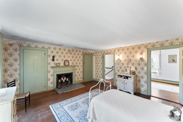 bedroom with a fireplace with raised hearth, a baseboard radiator, wood-type flooring, baseboards, and wallpapered walls