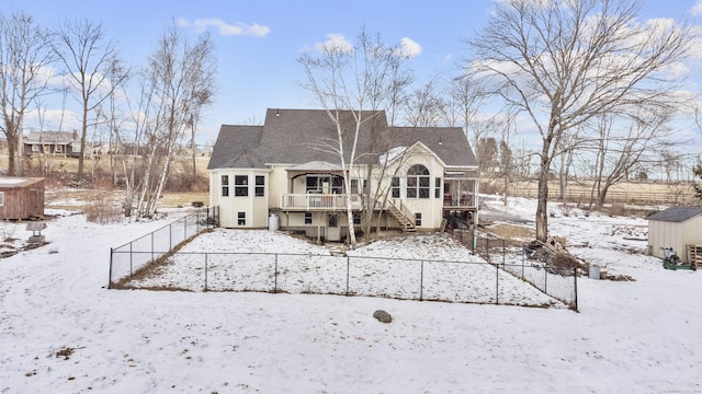 snow covered back of property featuring a wooden deck and a storage shed