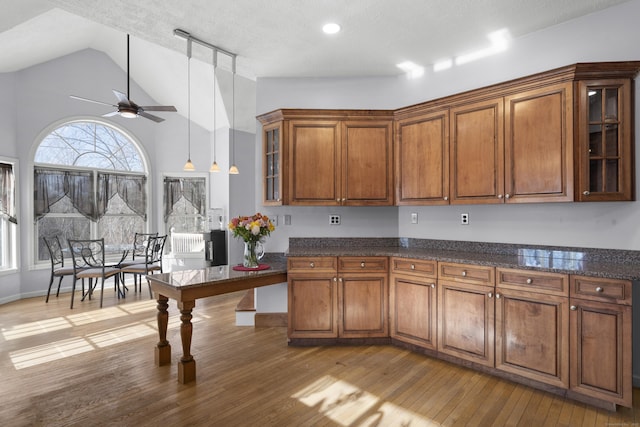 kitchen with vaulted ceiling, pendant lighting, light wood-type flooring, ceiling fan, and a textured ceiling