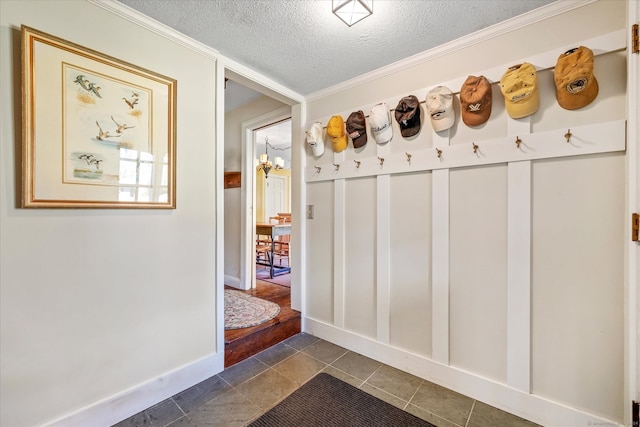 mudroom featuring dark tile patterned floors, an inviting chandelier, a textured ceiling, and ornamental molding