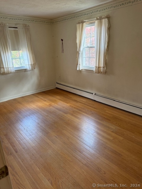 spare room with a baseboard radiator, a textured ceiling, and light wood-type flooring