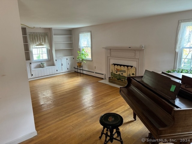 misc room with light hardwood / wood-style flooring, a healthy amount of sunlight, and a baseboard heating unit