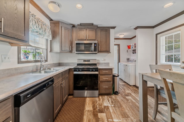 kitchen featuring sink, light hardwood / wood-style floors, crown molding, appliances with stainless steel finishes, and washer and dryer