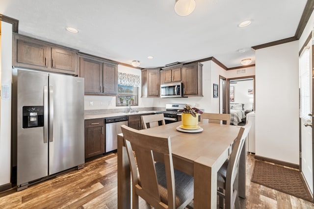 kitchen featuring appliances with stainless steel finishes, hardwood / wood-style flooring, crown molding, and dark brown cabinets