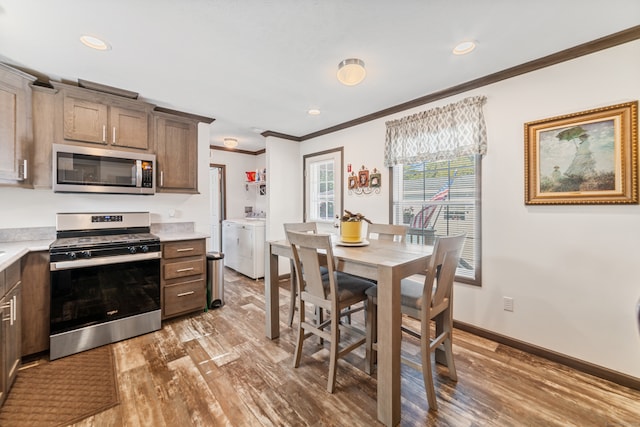 kitchen with independent washer and dryer, ornamental molding, appliances with stainless steel finishes, and hardwood / wood-style flooring