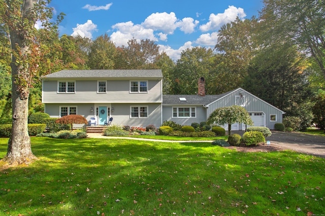 colonial house featuring an attached garage, aphalt driveway, a chimney, and a front yard