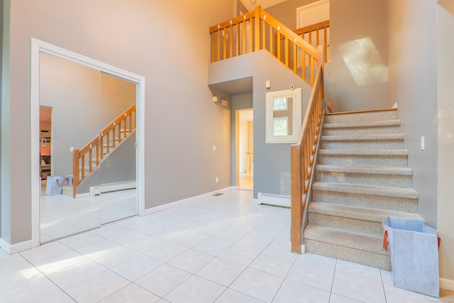 staircase with a high ceiling, a baseboard heating unit, and tile patterned flooring