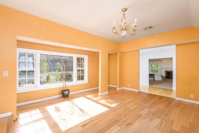 spare room featuring hardwood / wood-style flooring, lofted ceiling, a chandelier, and a healthy amount of sunlight