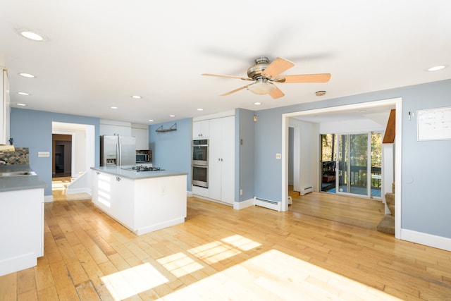 kitchen with white cabinets, a kitchen island, baseboard heating, stainless steel appliances, and light wood-type flooring