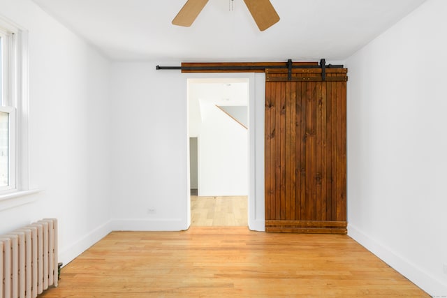 unfurnished room featuring ceiling fan, light wood-type flooring, a barn door, and radiator heating unit