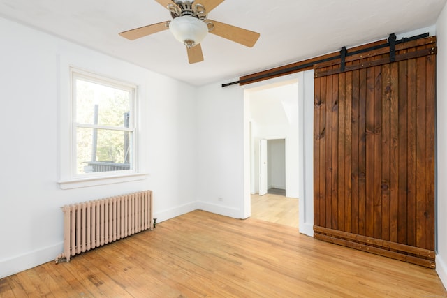 unfurnished room with a barn door, ceiling fan, radiator, and light hardwood / wood-style flooring