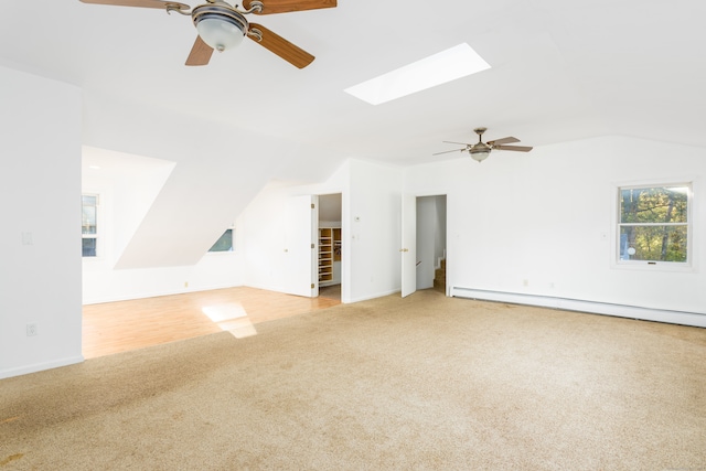 unfurnished living room with light carpet, ceiling fan, a baseboard heating unit, and vaulted ceiling with skylight