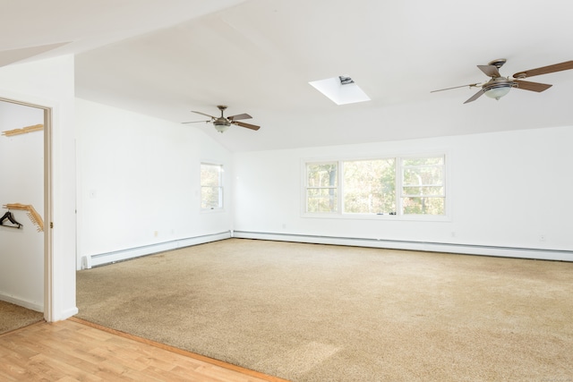 spare room with ceiling fan, a baseboard heating unit, vaulted ceiling with skylight, and light hardwood / wood-style flooring