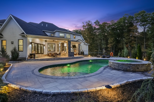 back house at dusk featuring ceiling fan, a pool with hot tub, and a patio