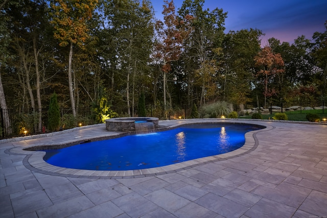 pool at dusk featuring a patio, an in ground hot tub, and pool water feature