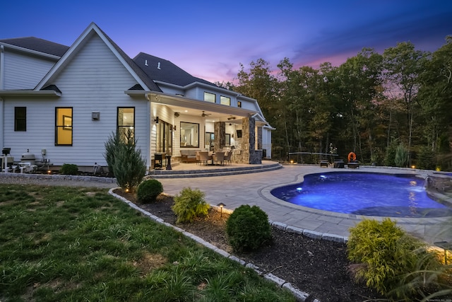 back house at dusk featuring ceiling fan, a pool with hot tub, a yard, pool water feature, and a patio area