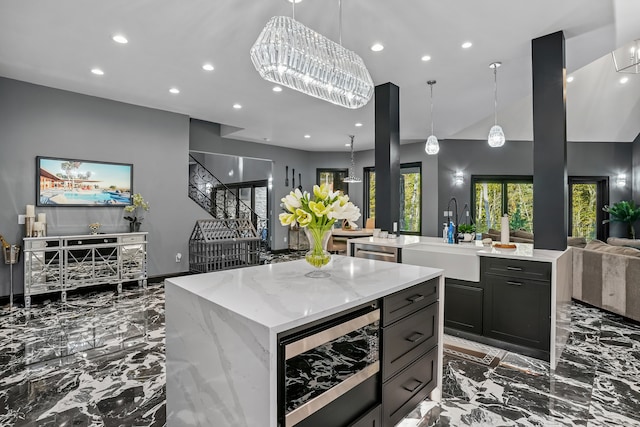 kitchen featuring wine cooler, sink, decorative light fixtures, a large island with sink, and light stone countertops