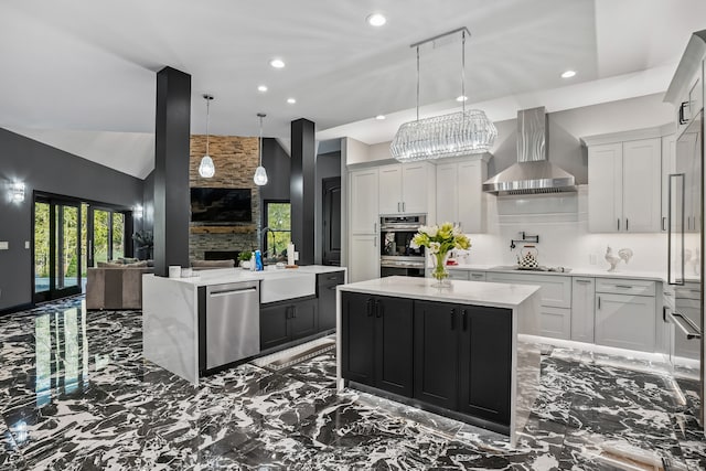 kitchen featuring sink, decorative light fixtures, wall chimney exhaust hood, stainless steel appliances, and a center island