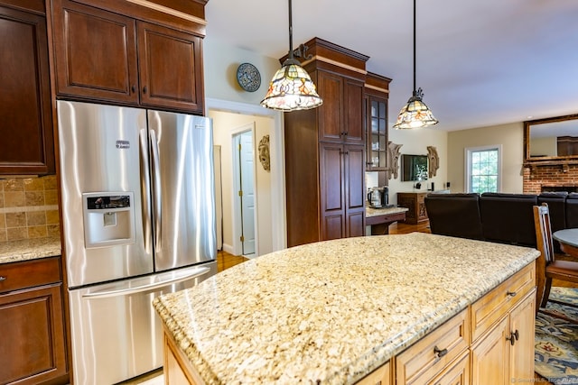 kitchen featuring tasteful backsplash, a brick fireplace, decorative light fixtures, stainless steel refrigerator with ice dispenser, and light stone countertops