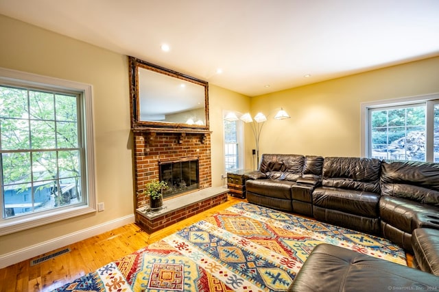 living room with wood-type flooring, a brick fireplace, and a healthy amount of sunlight