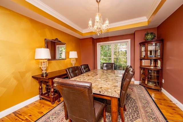 dining room featuring wood-type flooring, a tray ceiling, and ornamental molding