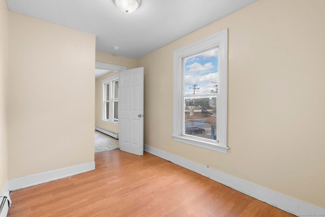 spare room featuring baseboard heating, light hardwood / wood-style flooring, and a wealth of natural light