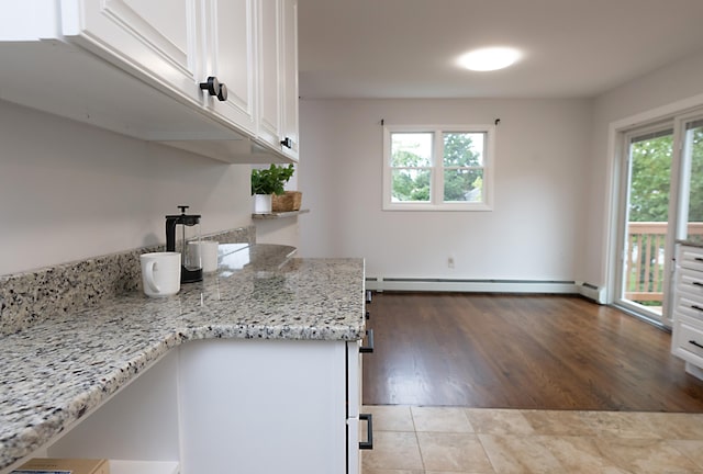 kitchen featuring white cabinetry, light stone countertops, a baseboard heating unit, and a wealth of natural light