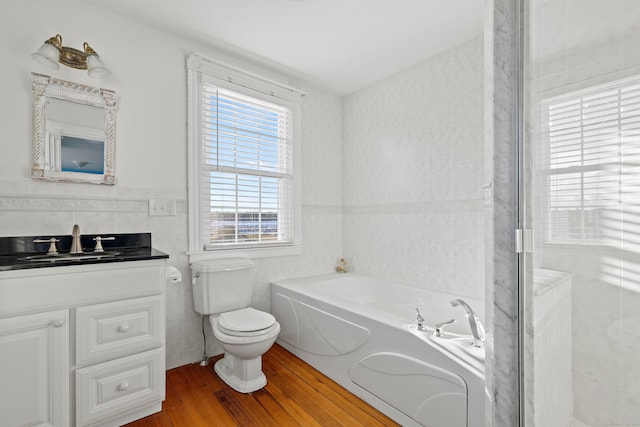 bathroom with vanity, wood-type flooring, a bath, tile walls, and toilet