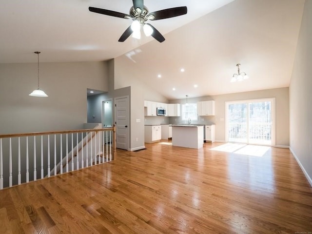 unfurnished living room with ceiling fan with notable chandelier, high vaulted ceiling, and light hardwood / wood-style flooring