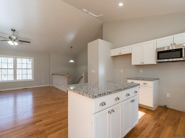 kitchen featuring light stone countertops, white cabinets, vaulted ceiling, and light hardwood / wood-style flooring