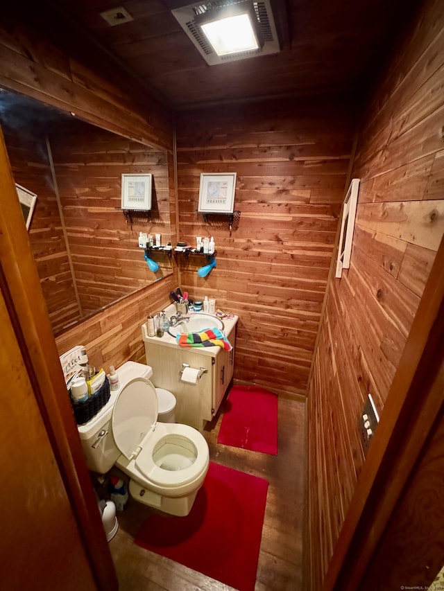 bathroom with vanity, toilet, and wood walls