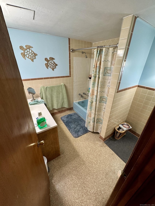 full bathroom with a wainscoted wall, shower / bath combination with curtain, a textured ceiling, and tile walls