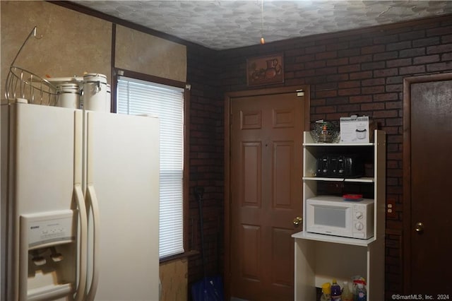 kitchen with white appliances, brick wall, and a textured ceiling