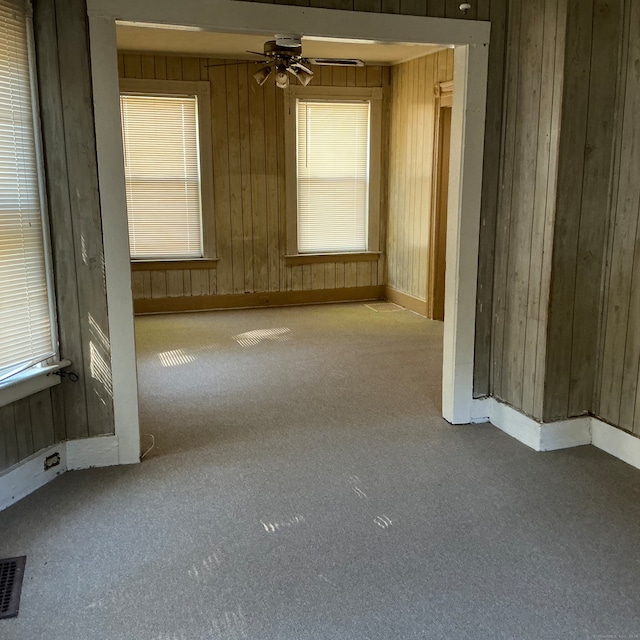 empty room featuring carpet flooring, wooden walls, and ceiling fan