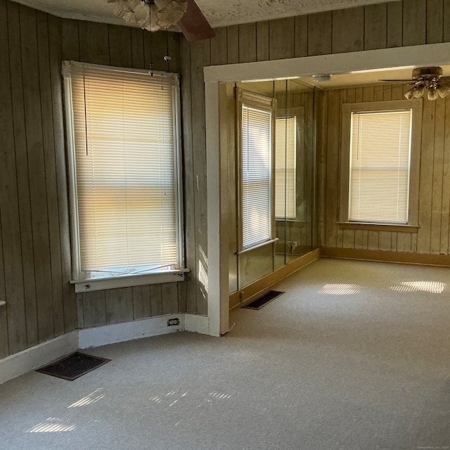 carpeted empty room featuring ceiling fan and wood walls