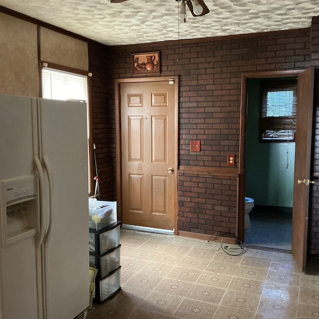 interior space featuring brick wall, white fridge with ice dispenser, a textured ceiling, and ceiling fan