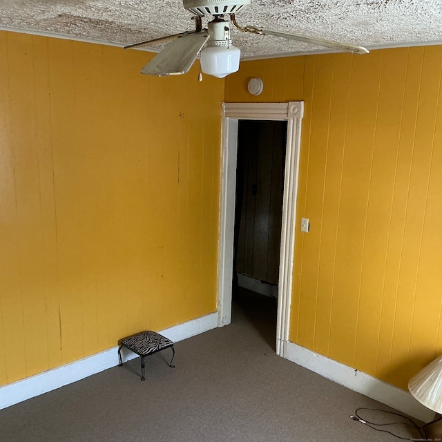 carpeted spare room featuring ceiling fan, wood walls, and a textured ceiling