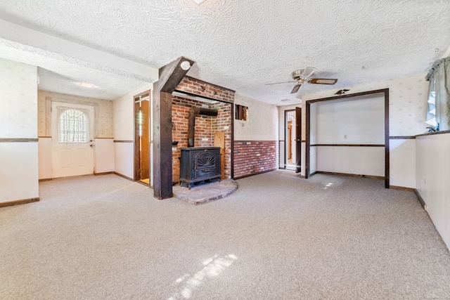 unfurnished living room with light carpet, a textured ceiling, and a wood stove