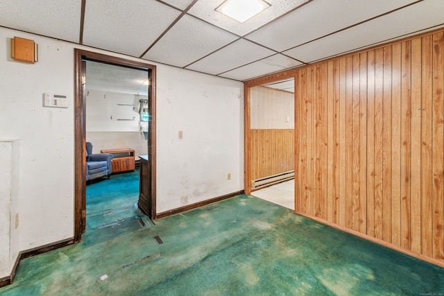 spare room with a paneled ceiling, wood walls, carpet flooring, and a baseboard heating unit